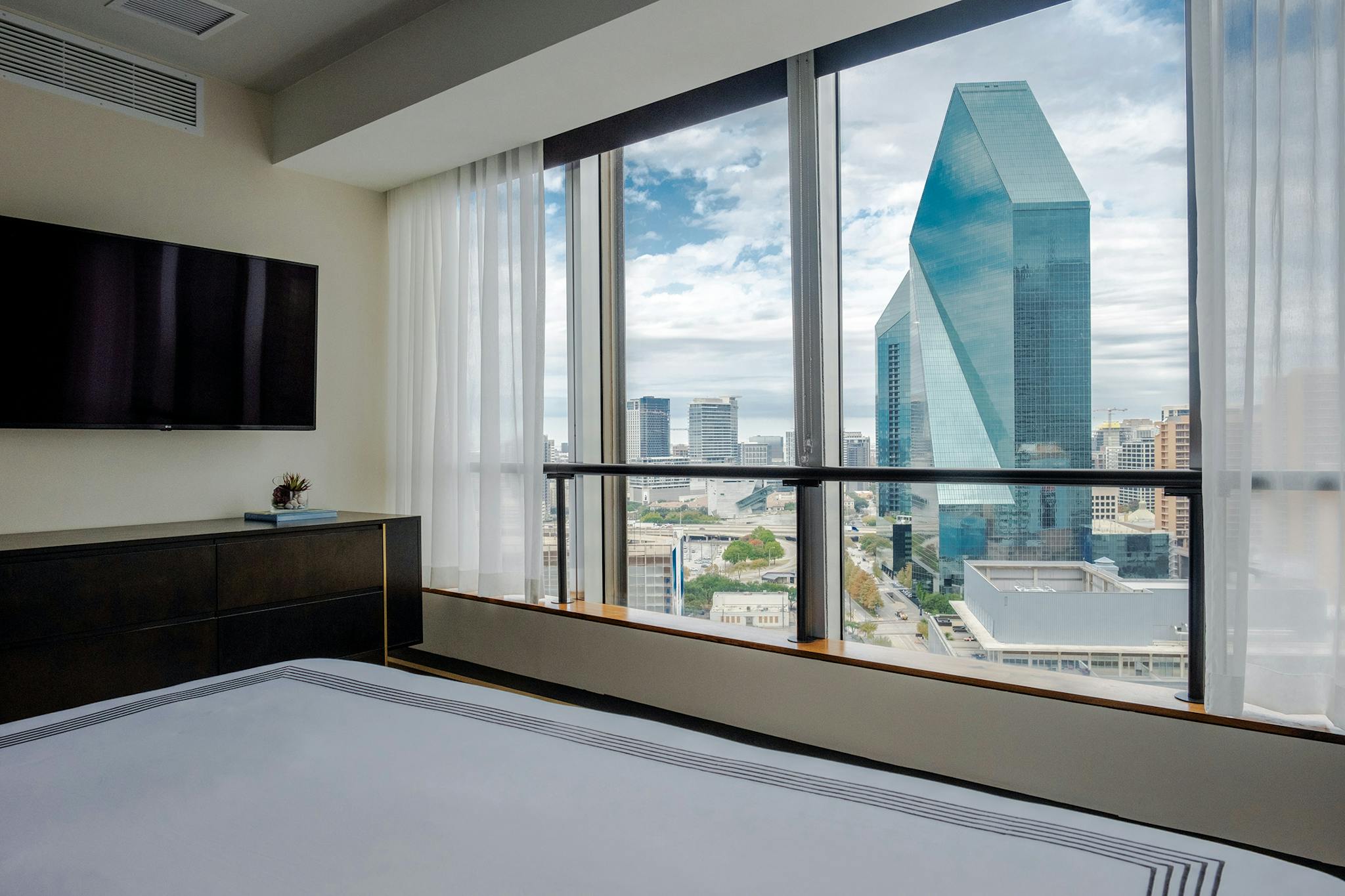 A hotel room with floor-to-ceiling windows displaying downtown Dallas.