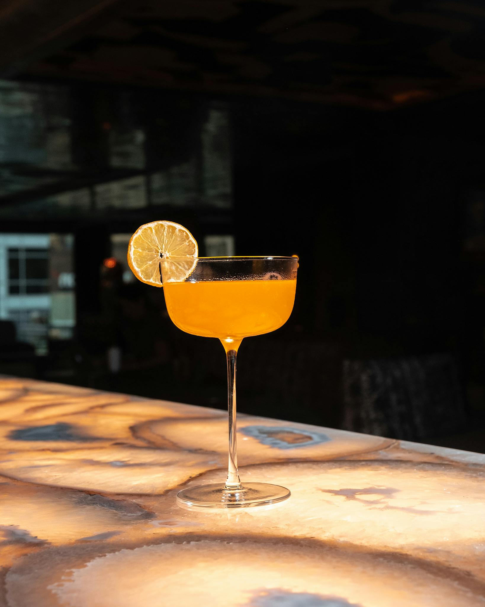 An orange cocktail with a lemon garnish atop Catbird's bar counter.