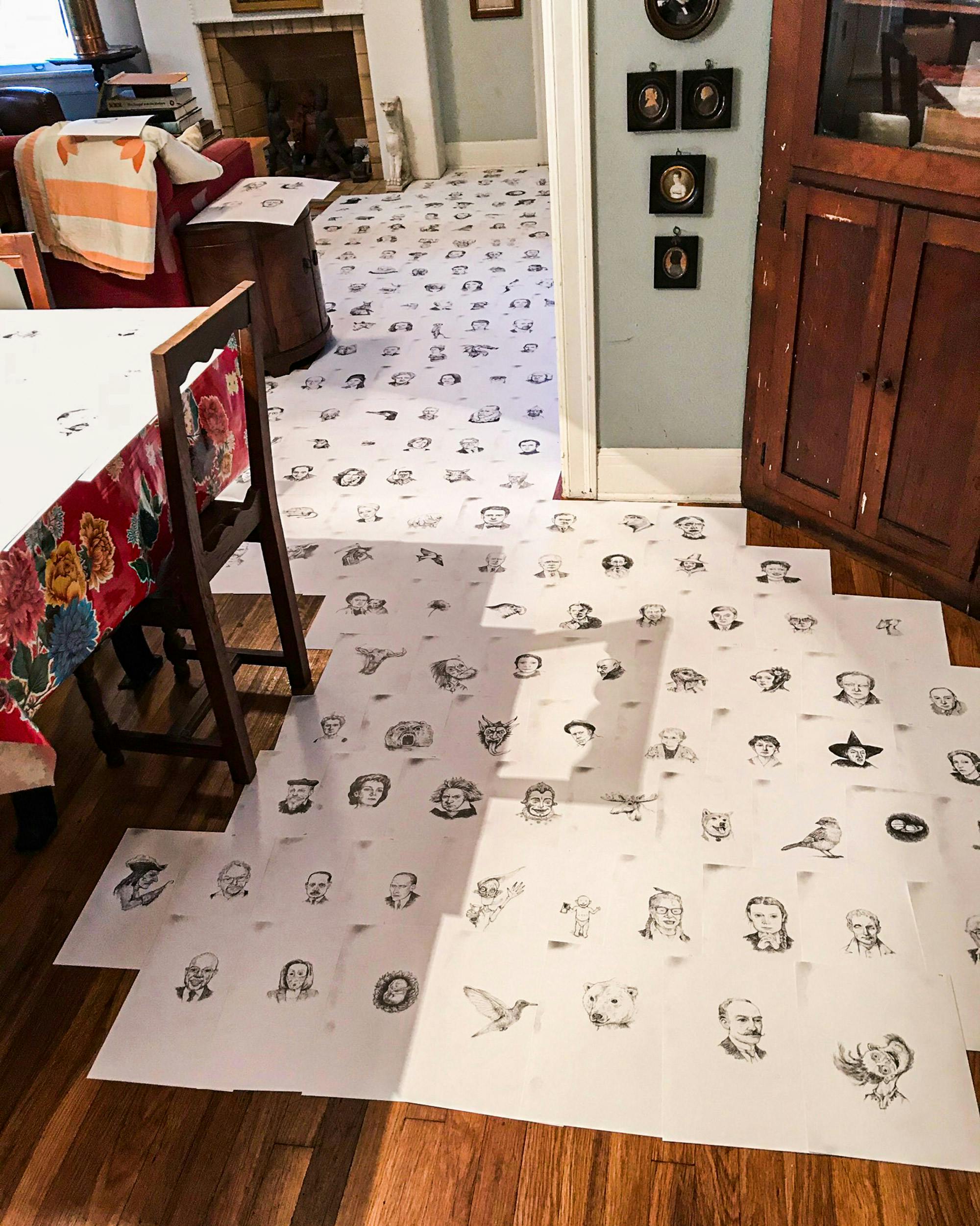 A collection of Edward Carey sketches laid out on his wood floor. 