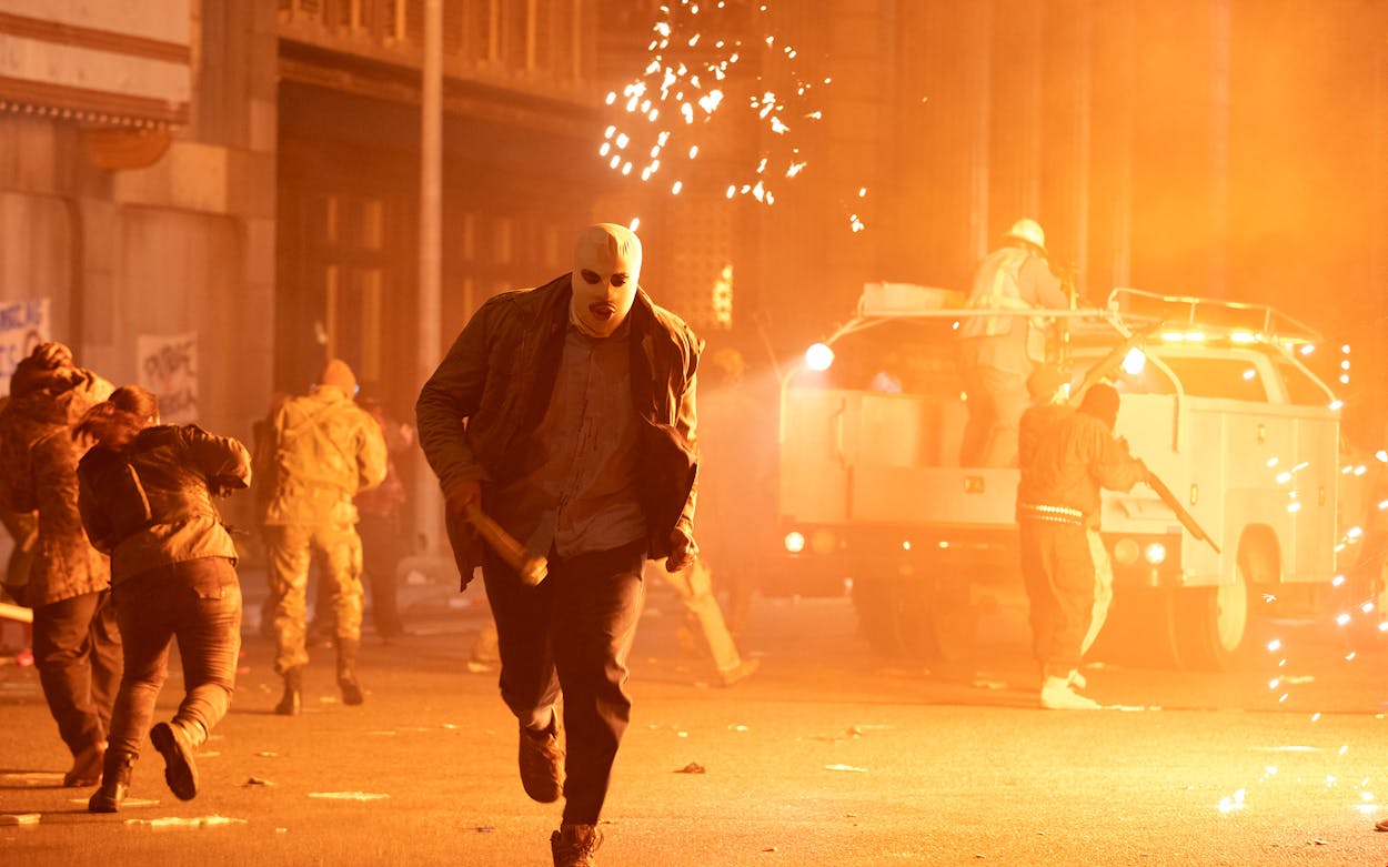 Screenshot of a masked man running from an explosion from 'The Forever Purge.'