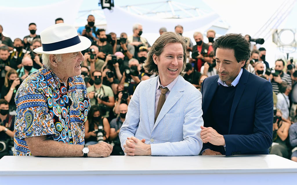 Bill Murray, Wes Anderson, and Adrien Brody in front of reports. 
