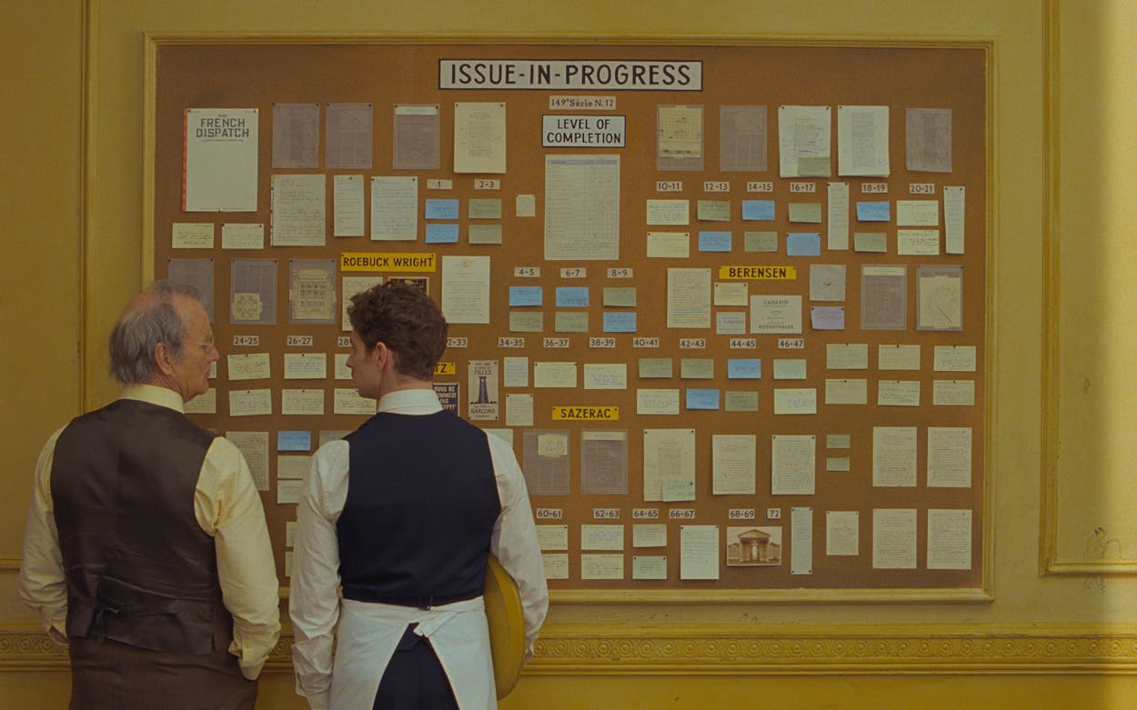 French Dispatch still of Bill Murray and Pablo Pauly looking at a bulletin board.