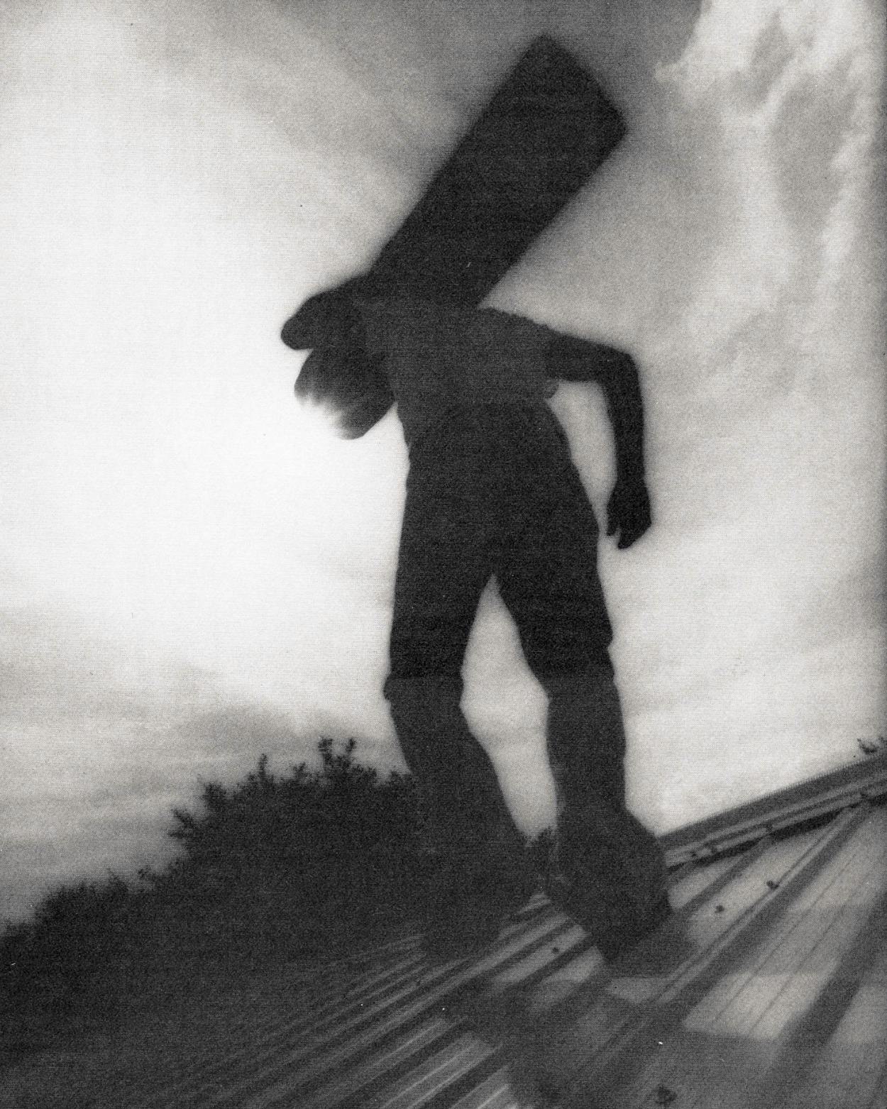 A man walks across a rooftop with a beam over his shoulder and his back to the camera.