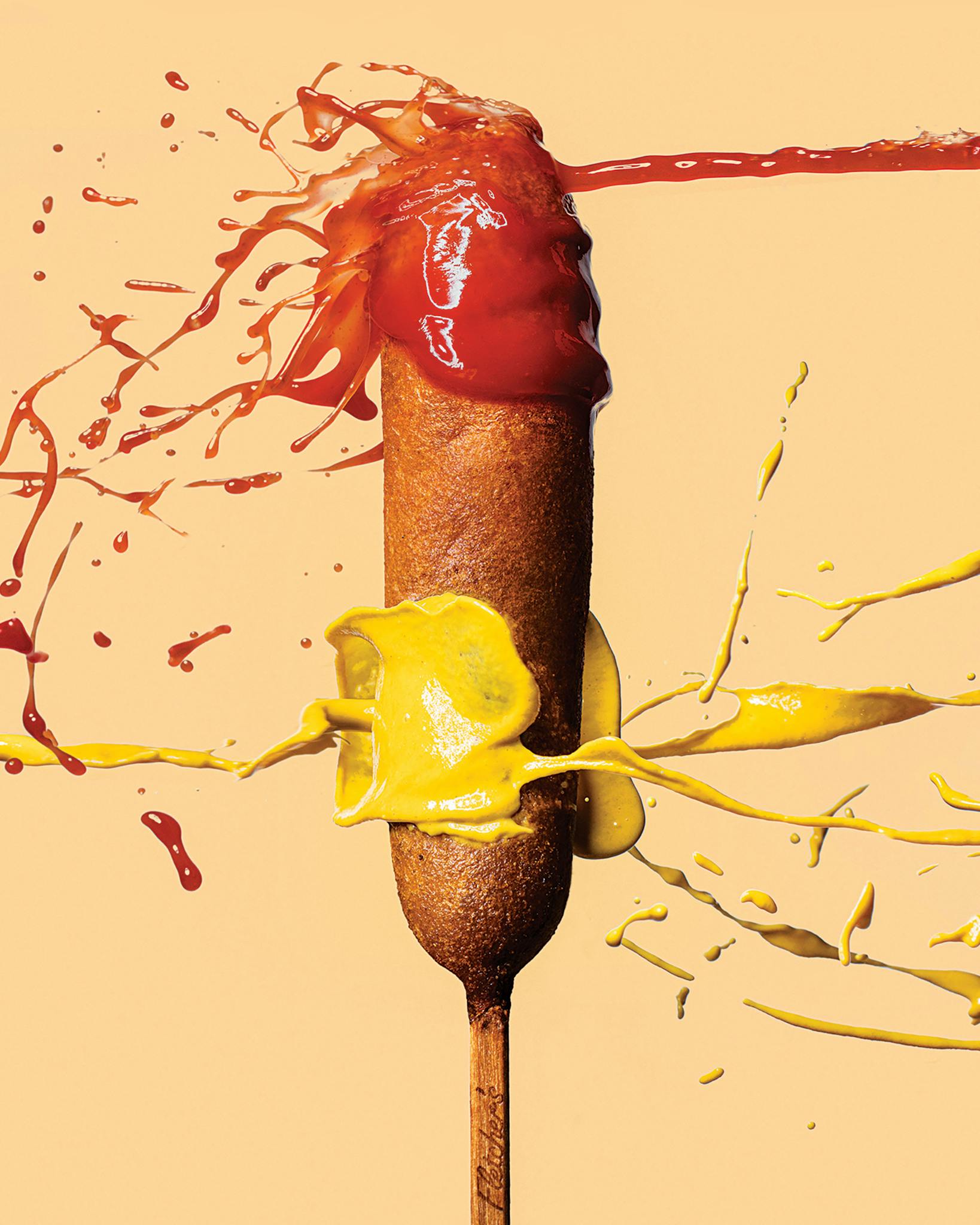 Ketchup and mustard are aggressively squirted on a corny dog from opposing sides.