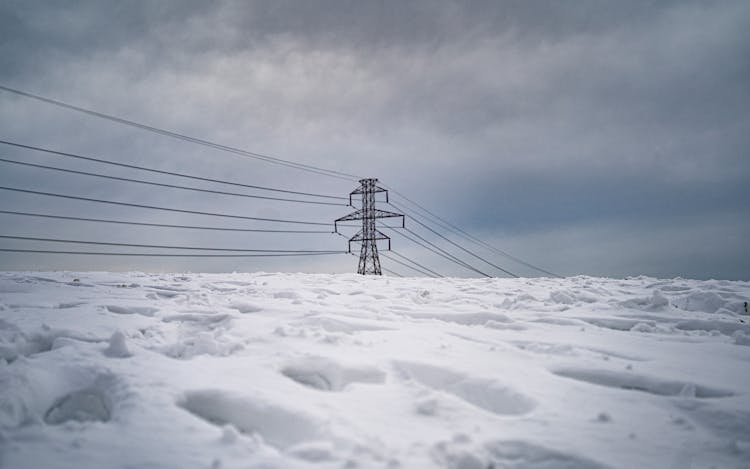 Snow with footprints covers the foreground, with power lines in the background against an ominous, cloudy sky.
