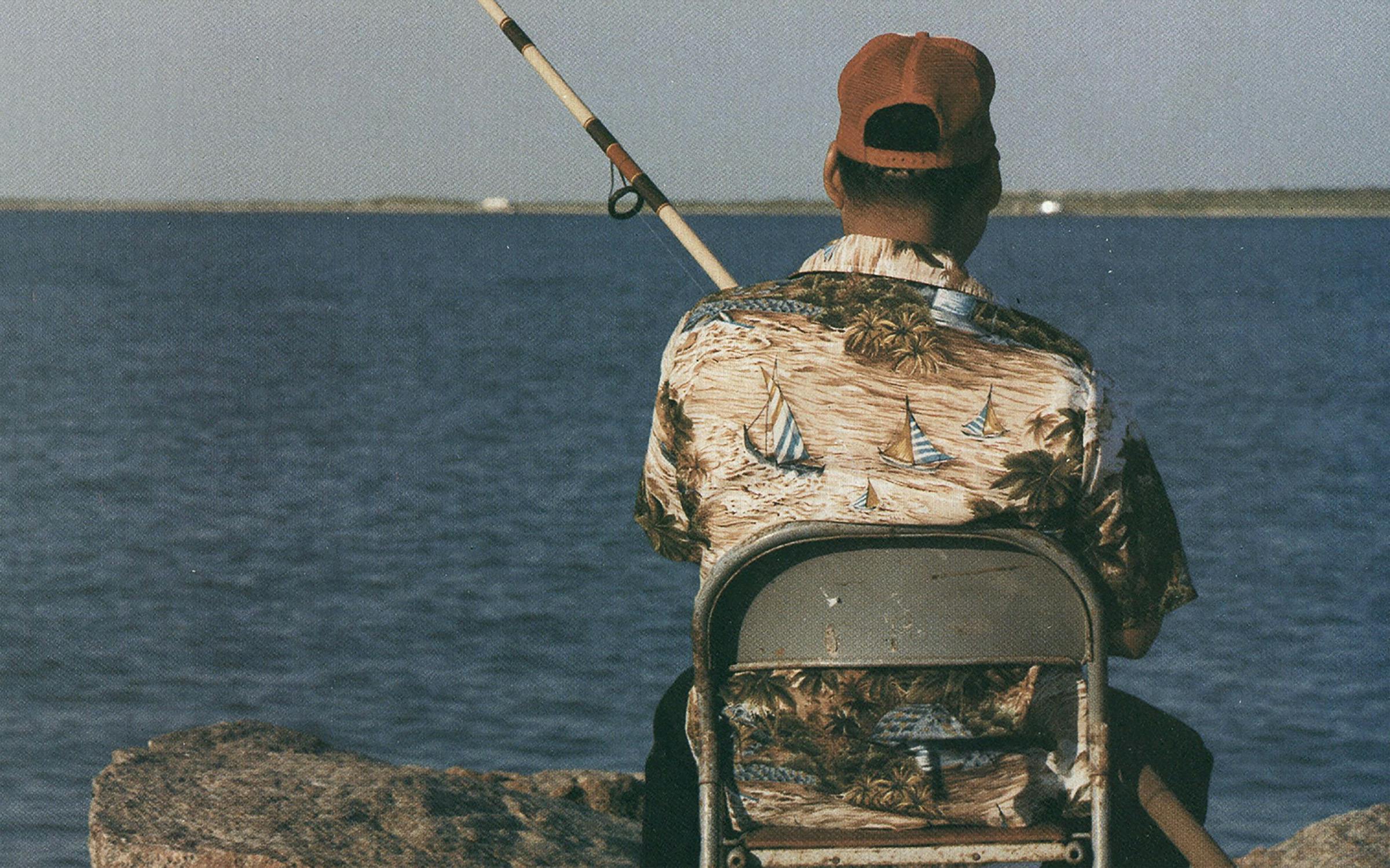 A father with a fishing rod on his shoulder standing on the edge of the  shore