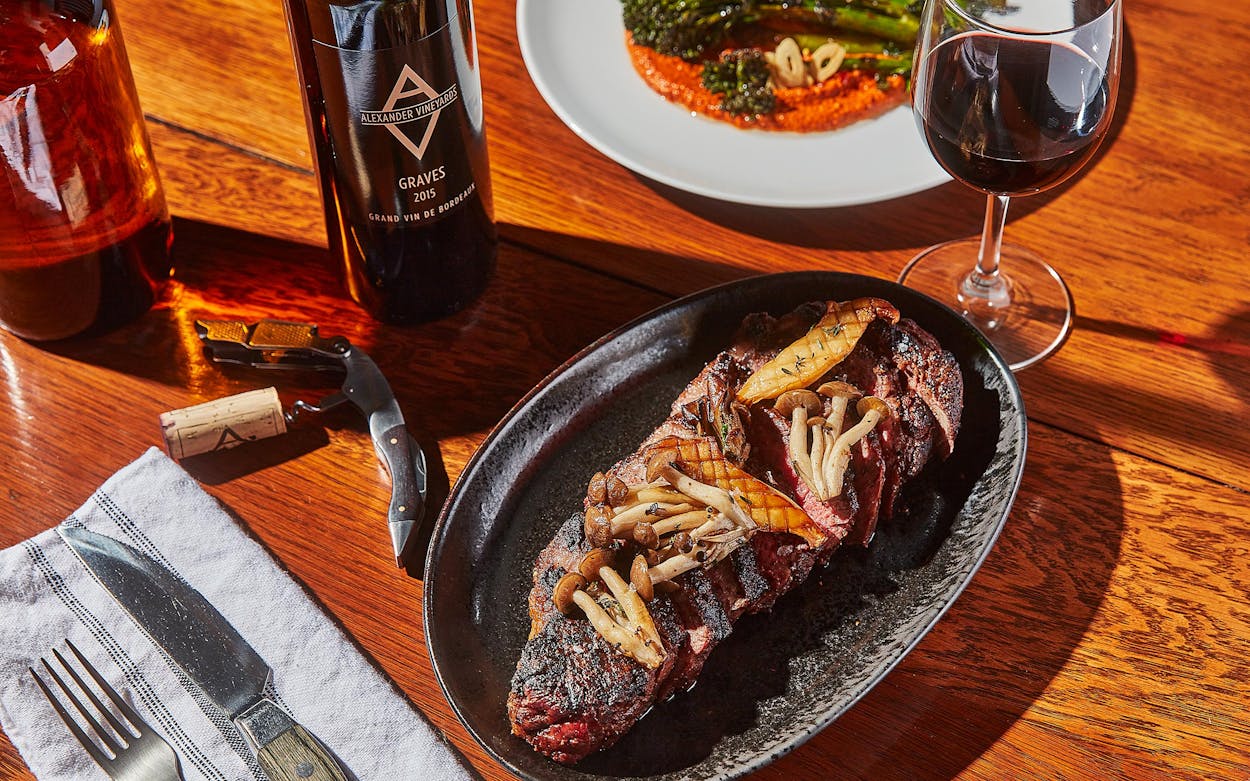 The wood-fired eighteen-ounce Akaushi New York strip steak, with sautéed mushrooms and a broccolini side, at Black Cur Steak.