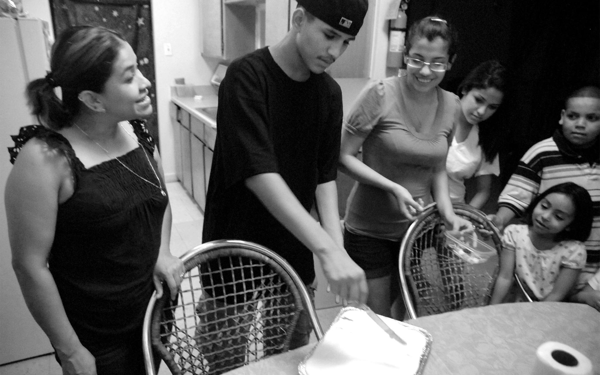 Christian cuts his own birthday cake, a tres leches, as his mother Maricela, left, sister Arleen, right, girlfriend Alexia Aleman, third from right, an unidentified person, second from right, and friend Miguel “Junior” Umanzor Jr. watch in their apartment at Booker T. on July 16, 2009. Christian was celebrating his fourteenth birthday, which would be his last.