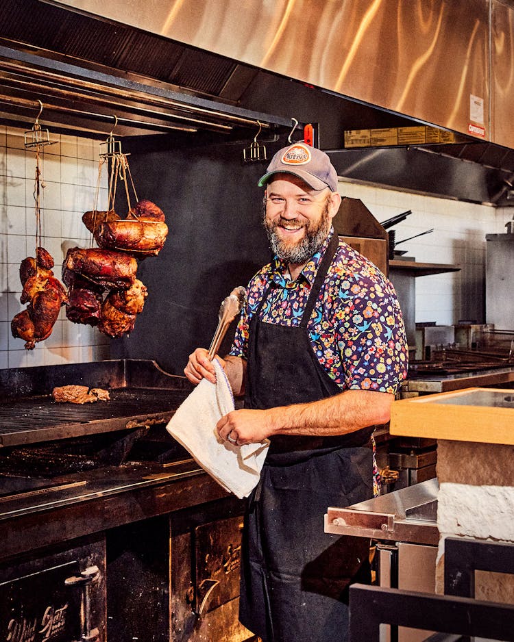 Chef Nick Fine in the kitchen at Wild Oats, with whole chickens hanging over their live fire grill.
