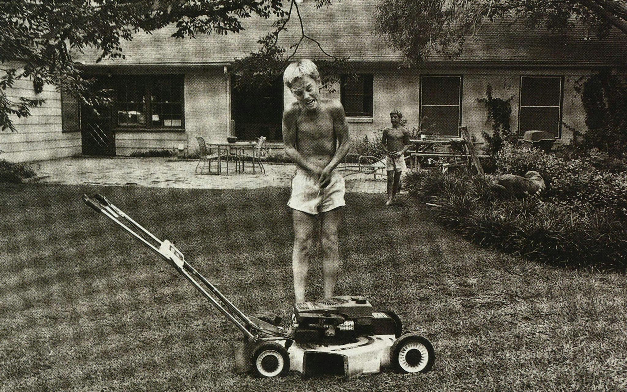 Owen and Luke Wilson stand behind a lawn mower in their front yard.