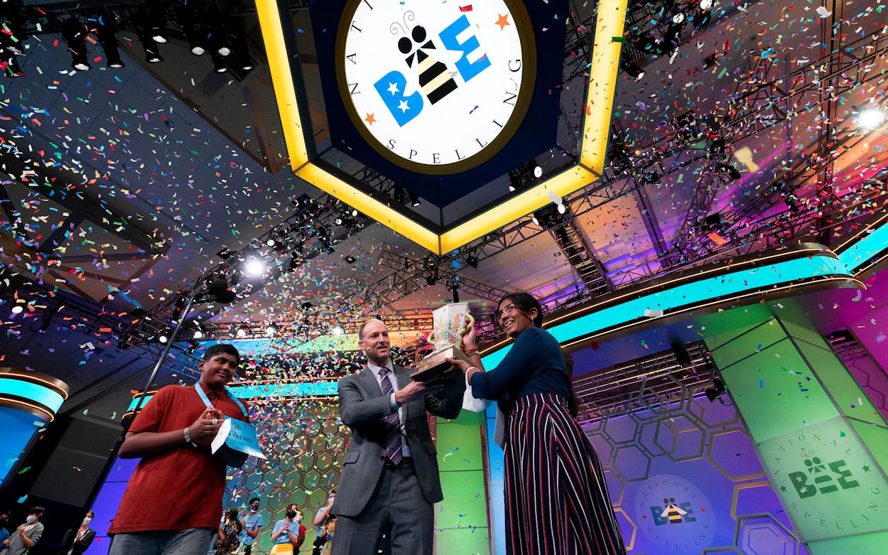 Harini Logan, 14, from San Antonio, Texas, receives her trophy from President and CEO of Scripps Company Adam Symson, after winning the Scripps National Spelling Bee competition, as second place Vikram Raju, 12, from Aurora, Colo., left, looks on, Thursday, June 2, 2022, in Oxon Hill, Md.