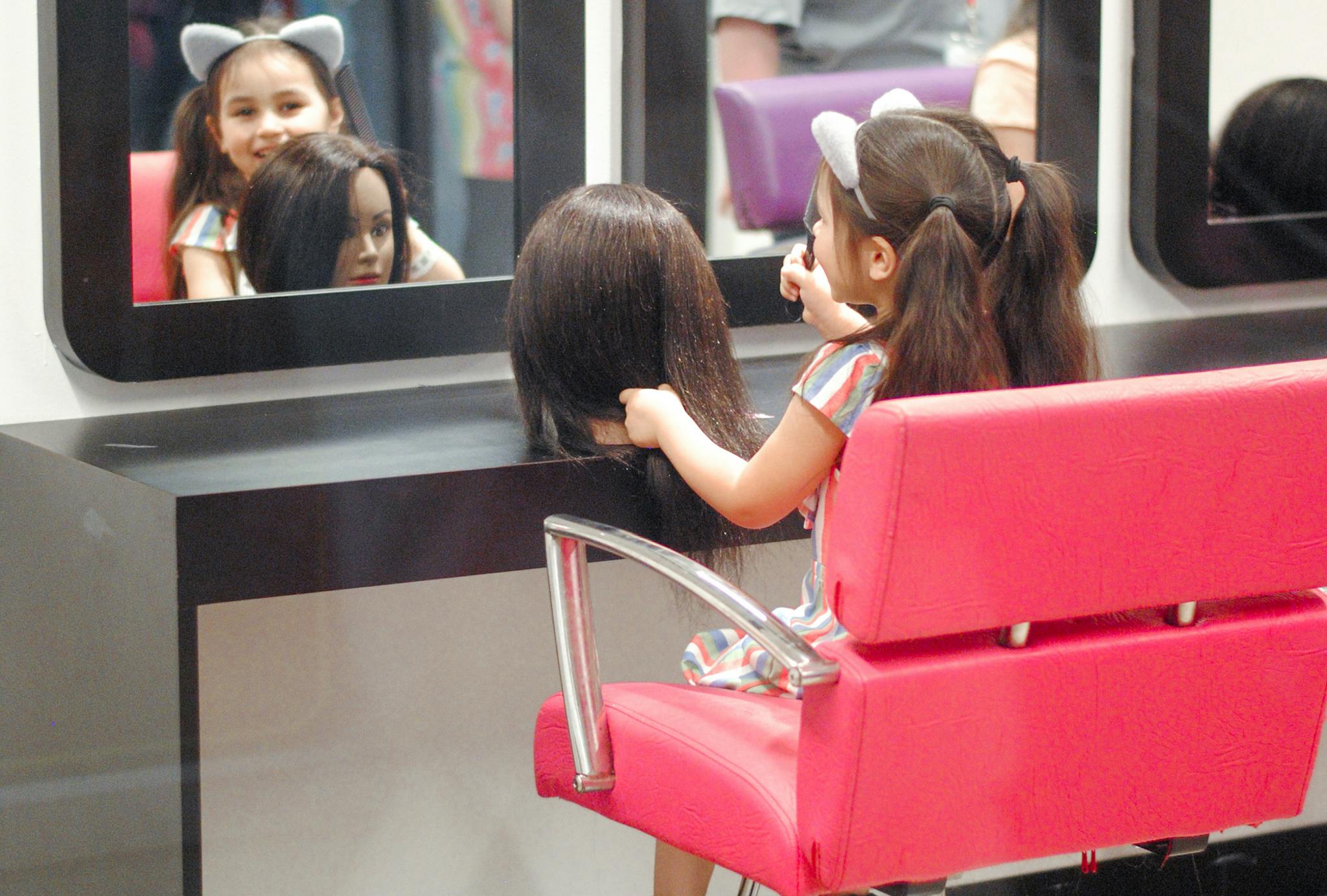 A little girl does the hair of a mannequin in a play beauty salon at Kidzania.