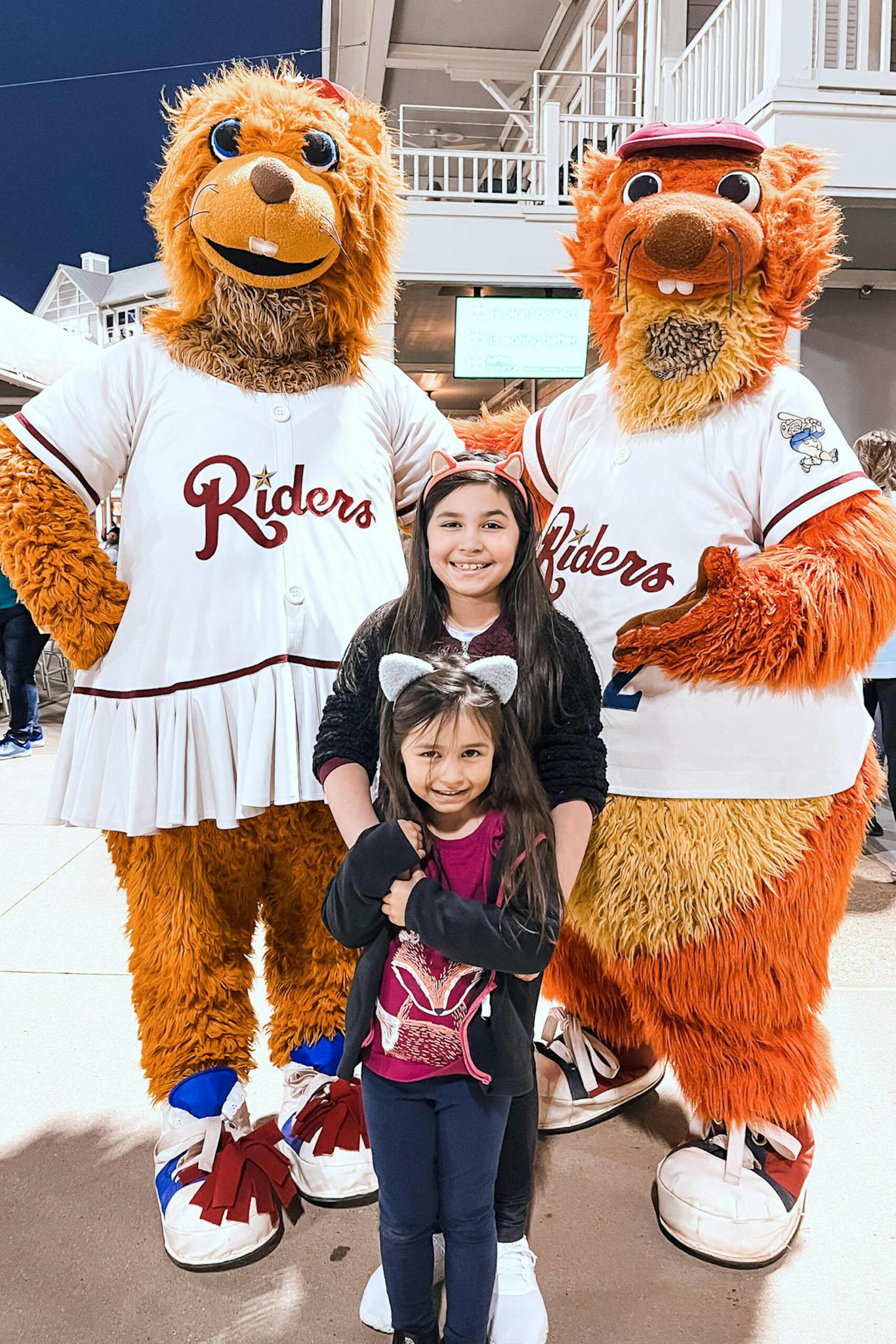 Two girls pose with the Frisco RoughRiders mascots.
