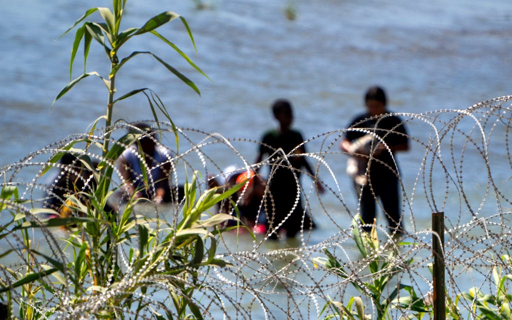 Migrants walk behind concertina wire in the water along the Rio Grande border with Mexico in Eagle Pass, Texas, on July 15, 2023. The buoy installation is part of an operation Texas is pursuing to secure its borders, but activists and some legislators say Governor Greg Abbott is exceeding his authority.