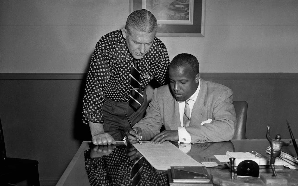 Claude Buddy Young, star halfback for the Dallas Texans, National Professional Football League entry, signs his 1952 contract, as Texans Head Coach Jim Phelan looks on, May 7, 1952, Dallas, Texas.