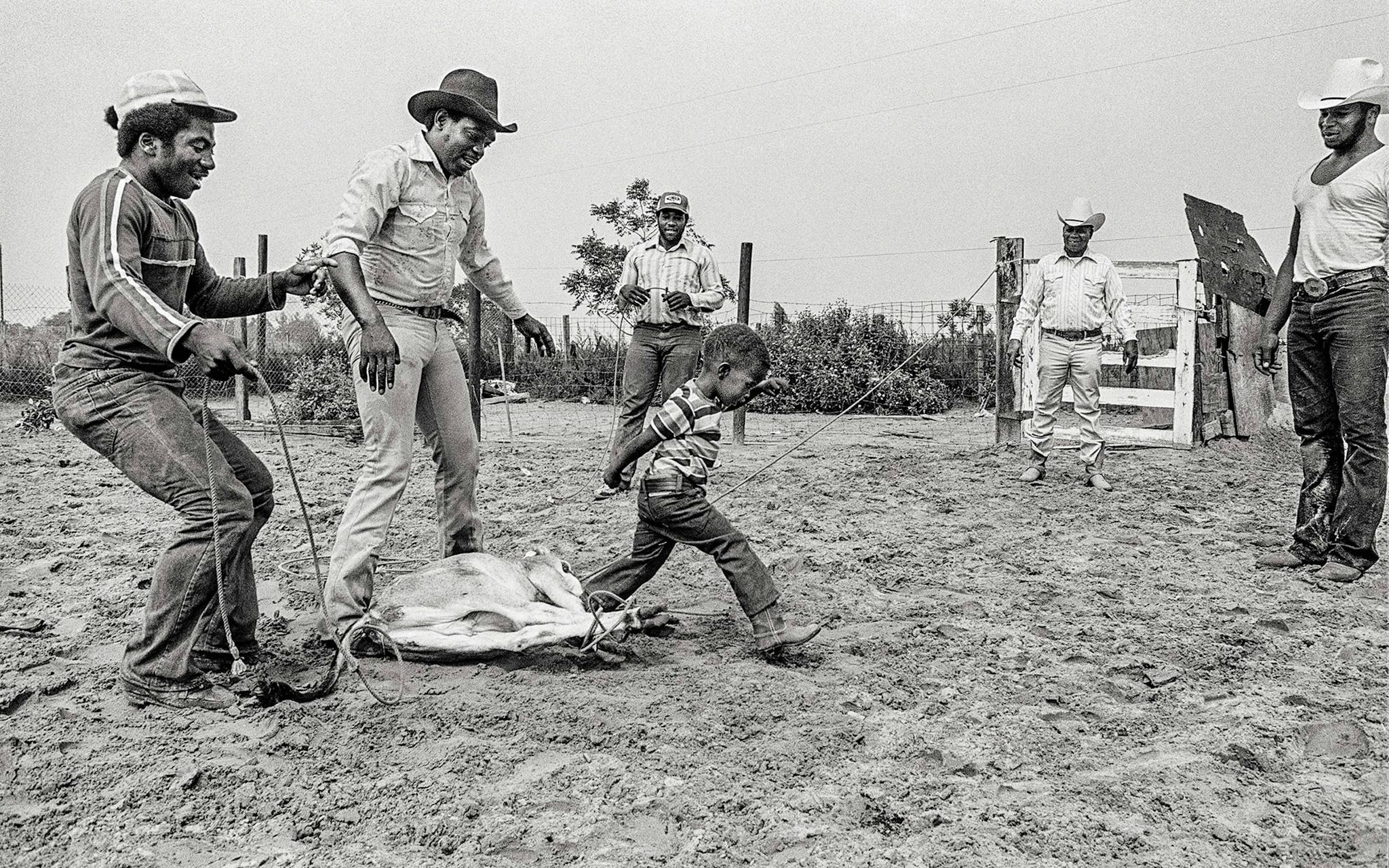 Rufus Green Sr. (far right) teaching his grandson the finer points of tying down a calf, in Hempstead, in 1977.