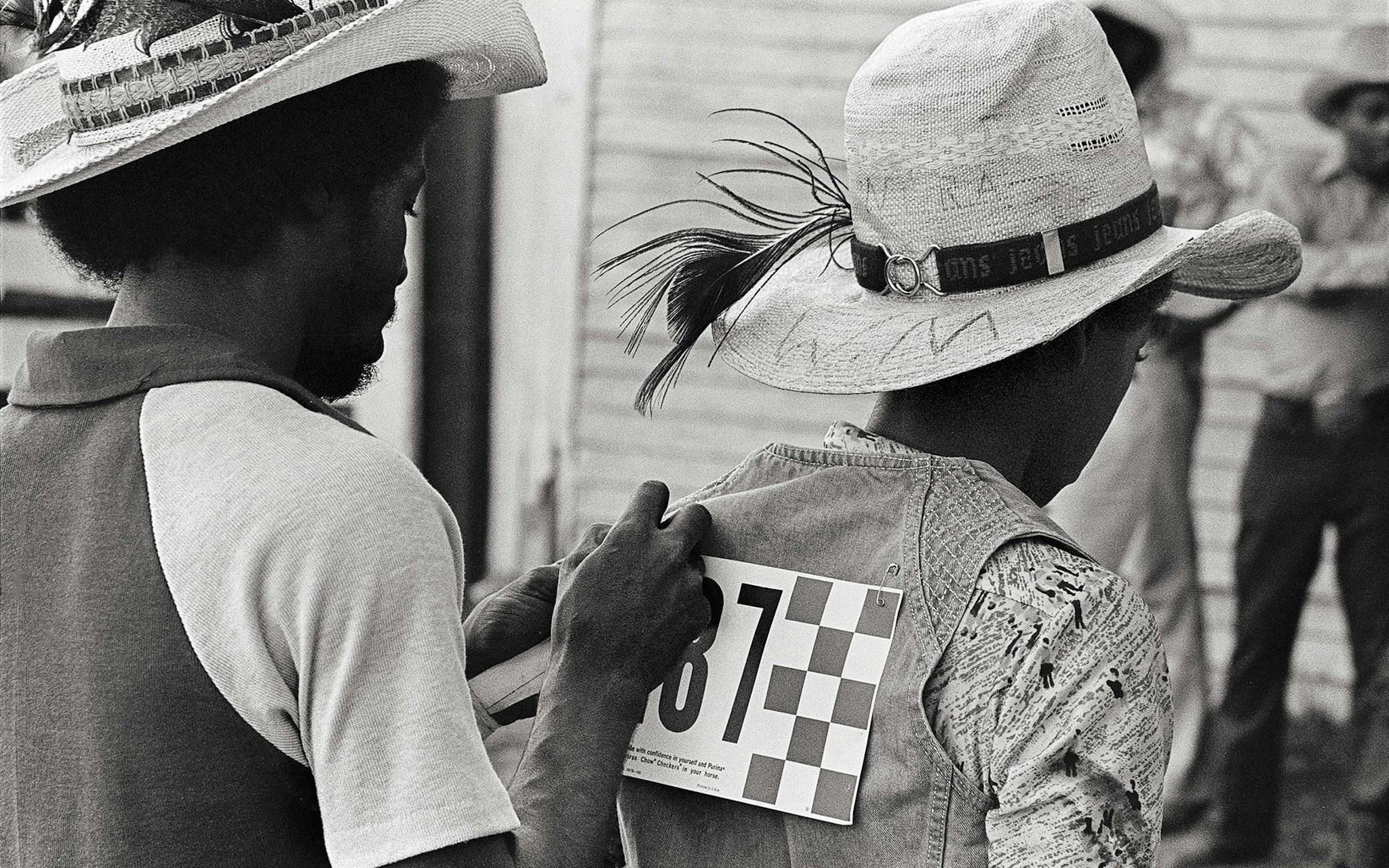 At the Diamond L arena in the summer of 1978, a couple of bronc riders helping each other pin on their contestant numbers.